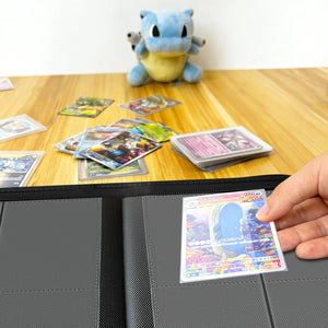 Hand placing a holographic Pokemon card into a binder on a wood table beside a Squirtle plush and scattered cards