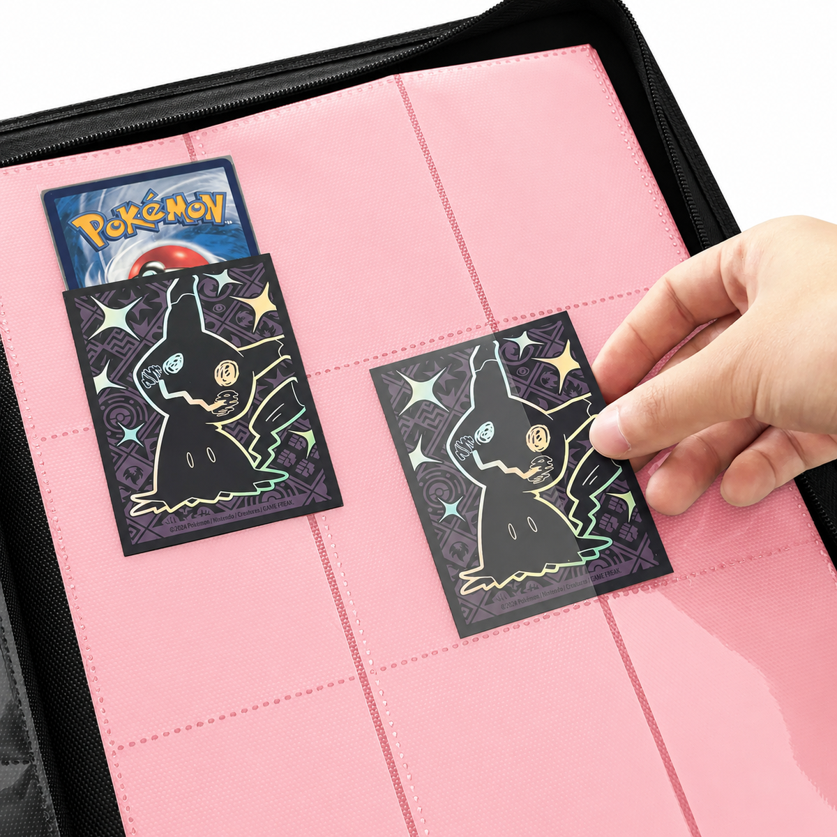 Hand sliding a double-sleeved card into a pink 9-pocket side-loading page of a Pokemon card binder