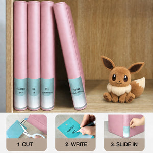 Pink card binders on a shelf with cut, write, and slide-in spine labels beside an Eevee plush