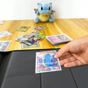 Hand placing a holographic Pokemon card into a binder on a wood table beside a Blastoise plush and scattered cards