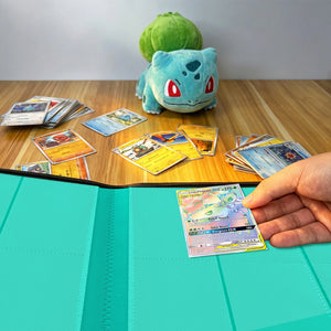 Collector placing holographic Pokemon card into 9-pocket binder beside scattered trading cards